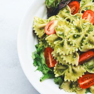 Pesto pasta with sliced tomatoes served on white ceramic plate