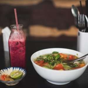 bowl of soup on black surface near bottle filled with pink liquid