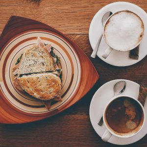 ham sandwich on plate near cappuccino on mug and coffee