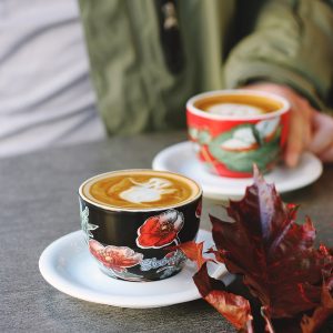 selective focus photo of black floral cup on white saucer with latte