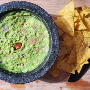 a bowl of guacamole next to a bowl of tortilla chips