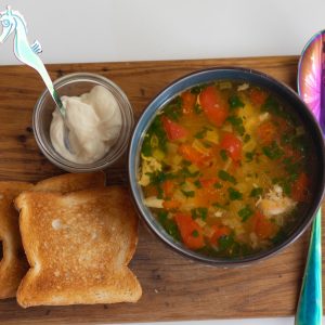 a bowl of soup and a spoon on a cutting board