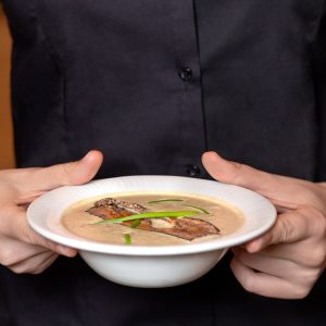 person holding white ceramic bowl with soup