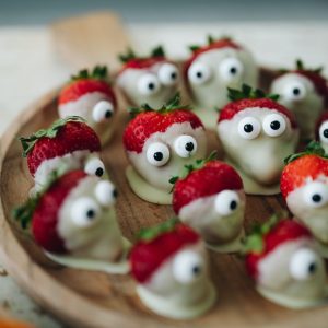 a wooden plate topped with strawberries covered in googly eyes