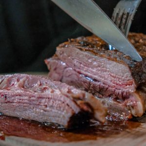 person slicing juicy medium rare meat on top of brown wooden cutting board