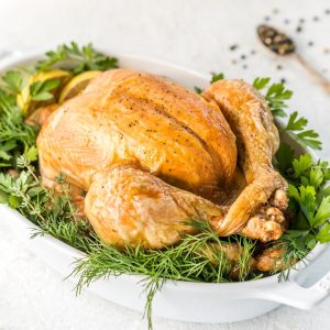 a roasted turkey in a white dish with fresh herbs